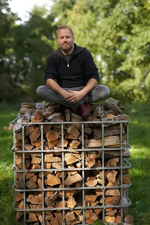 Daniel Reinhold sitzt auf einer Gitterbox voller Brennholz