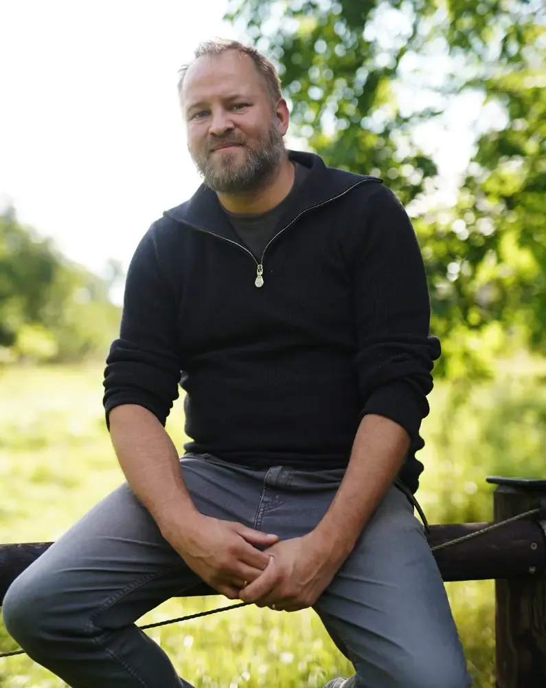Daniel Reinhold sitzt lässig auf einem Weidezaun auf seinem Hof